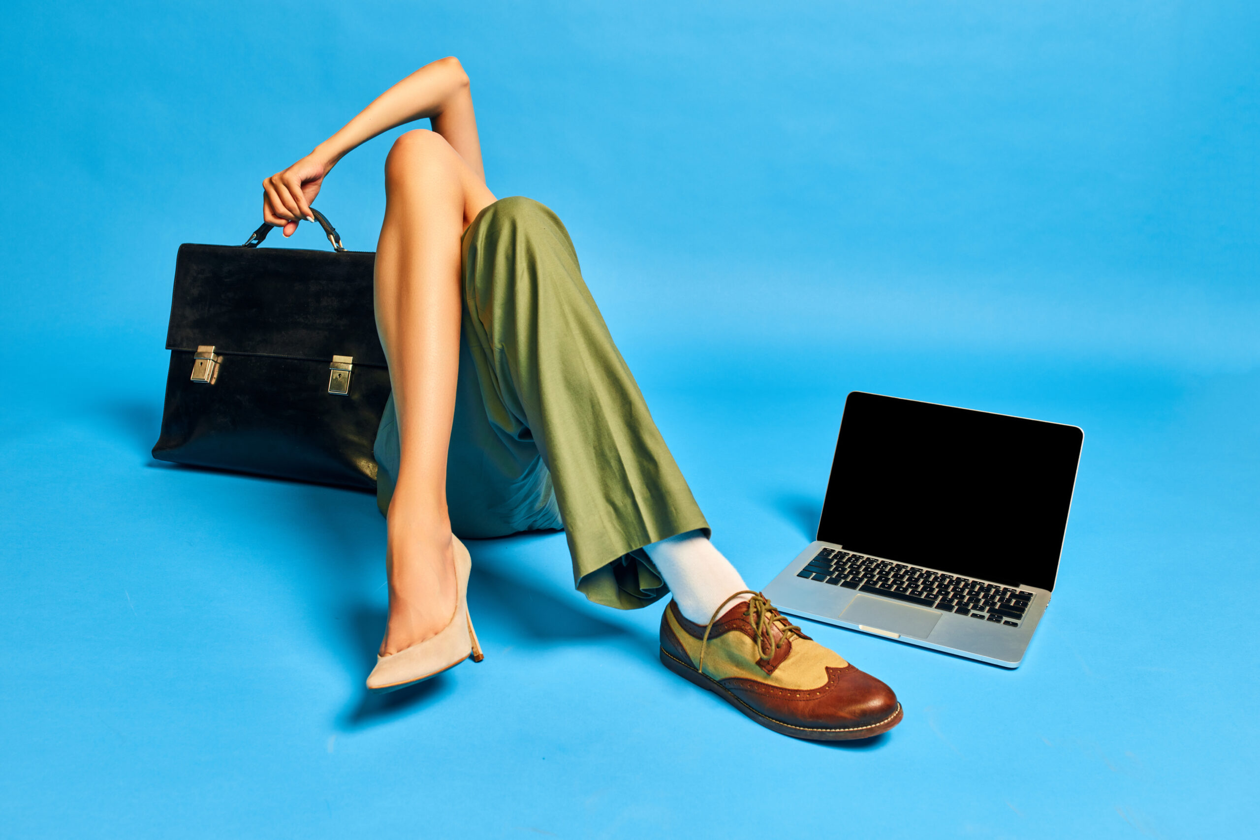 Teamwork. Male and female body parts. Legs in boots and heels with briefcase and laptop against blue studio background. Concept of creativity, business, fashion, surrealism, imagination, ad. Pop art